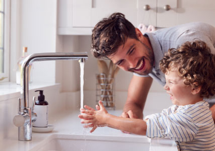 Ein Mann und ein Kind waschen sich in einer Küchenspüle mit Trinkwasser die Hände.